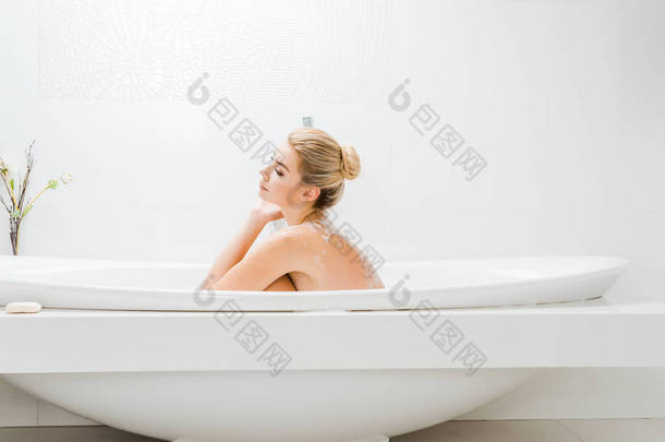 <strong>美丽</strong>和金发碧眼的女人洗澡与泡沫在浴室的侧视图 