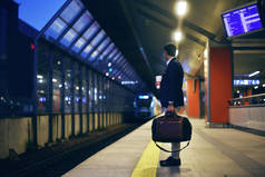 一名喝咖啡的男子站在火车站, 背景是行驶中的火车。绅士站在火车站的站台上。商务旅行, 商人等待火车.