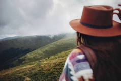 癖和旅游理念。女旅客手持帽子, 看着山。时髦的时髦女人带着背包, 集中在山上的云彩里。文本空间。大气矩
