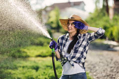 美丽的年轻园丁妇女浇水花园在炎热的夏天