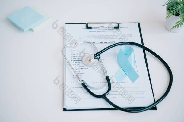 白桌子上的蓝色宣传带、医疗报告、听诊器和粘贴便条