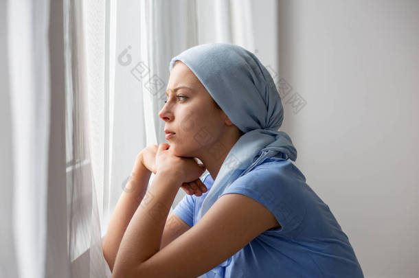 患有卵巢癌、戴着蓝色头巾、透过医疗中心窗户看的体贴年轻女孩