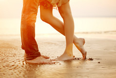 爱的年轻夫妇拥抱和亲吻在沙滩上在日落时分
