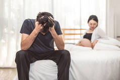 担心压力的男人坐在床上, 手放在额头上的卧室里, 情绪情绪严肃, 有孕妇的背景。主要抑郁障碍被称为 mdd 概念。物理保健