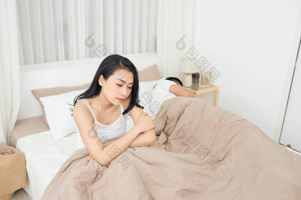 我们有一个问题。年轻人沮丧女孩坐<strong>在</strong>床上，对她的男朋友，躺<strong>在</strong>床上的<strong>边缘</strong>上.