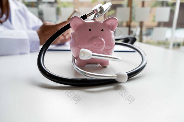 粉红储蓄罐，白色桌子上有医疗设备，护士坐在医疗概念和医疗保险的后面