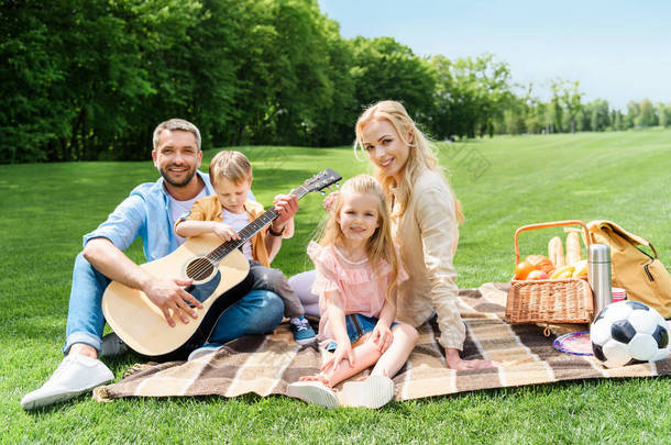 愉快的家庭与吉他微笑在照相机, 而坐在一起在<strong>格子</strong>在野餐