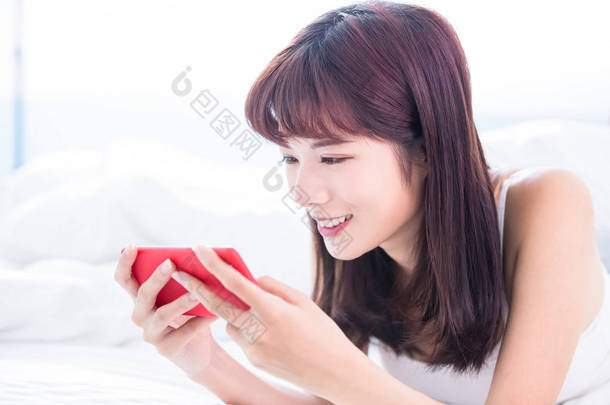 女人高兴地玩<strong>手机</strong>游戏或用智能<strong>手机看</strong>视频, <strong>躺</strong>在家里的床上
