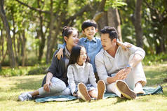 亚洲家庭与两个孩子有乐趣坐在草地上聊天在公园的户外聊天