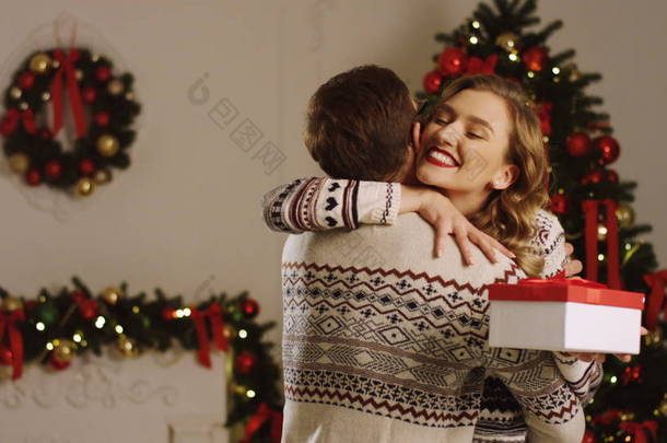 年轻情侣相爱有吸引力的人给他的迷人的女朋友在客厅里的灯在美丽的圣诞树附近的圣诞礼物。室内