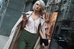 时尚。年轻时尚的女人走在城市街道上浏览互联网上的智能手机看一边沉思