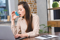 年轻女商人哮喘使用吸入器在办公室