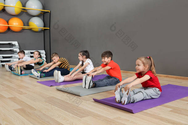 可爱的小孩子坐在地板上,在学校体育馆做体育锻炼。健康的生活方式