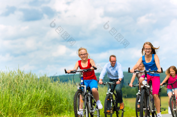 家庭在乡村景观的夏天骑自行车