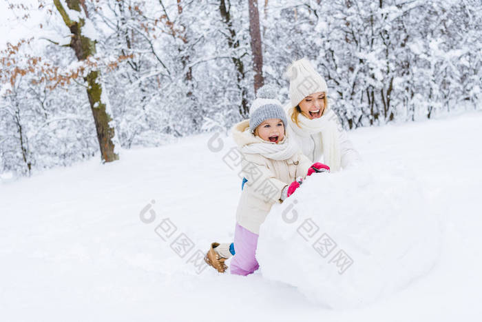 快乐的母亲和可爱的小女儿一起做雪人在冬天公园