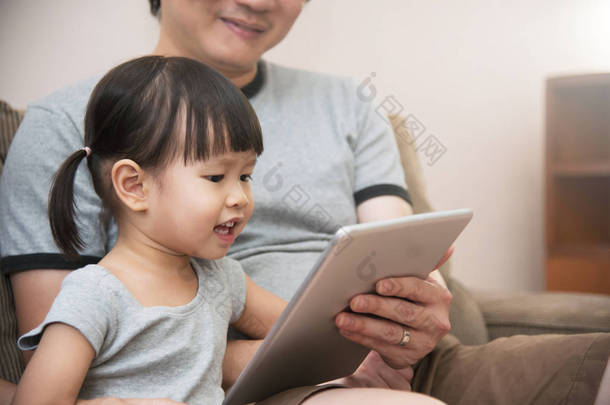 亚洲<strong>孩子</strong>和她<strong>父亲</strong>坐和使用数字平板电脑一起