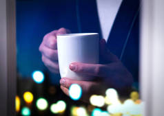 男人拿着咖啡杯在窗边。喝茶或热饮料。失眠或无法入睡。生病或患有流感。人在深夜醒来或清晨起床早在日出之前.