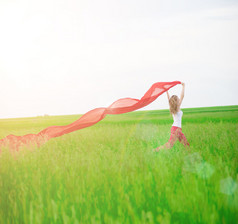 一位年轻的女士拿着纸巾在绿色的田野里奔跑。女人和红领巾。