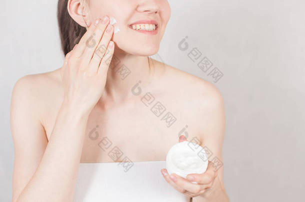 女孩在用白毛巾洗澡后, 把一罐奶油放在脸上。手的特写。概念美容护肤