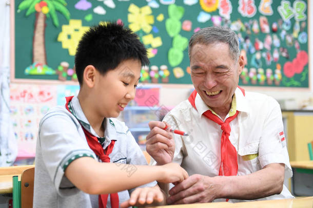 2018年5月28日，在中国东部江苏省南京市一所小学，一位身穿白衬衫、戴红领巾的老人在儿童节前与一名年轻学生合影。