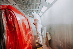 工人画一辆红色的汽车在一个特别的车库，穿着白色的衣服