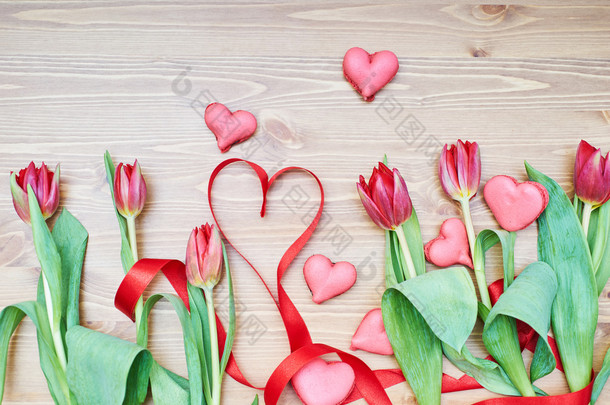 在木桌上放着鲜花和丝带的心形马卡龙。情人节创意装饰