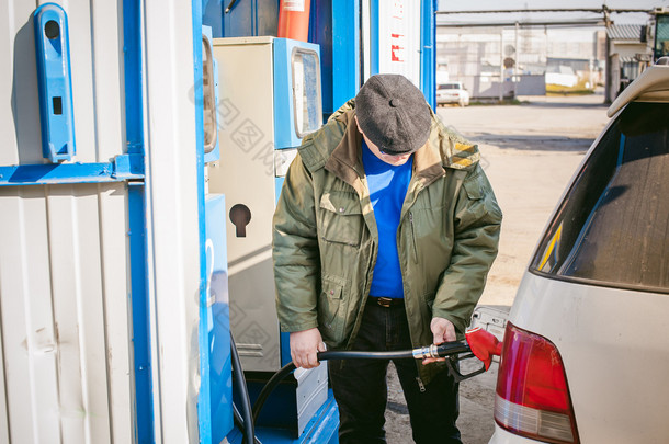 男子在一个加油站填充车辆油箱燃料。成年男子与一个小胡子和眼镜，加油前长途旅行的道路上向非网络加油站汽车