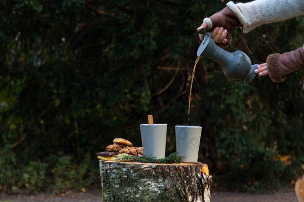 在森林里野营生活方式。在毛皮手套的女人倒在陶瓷杯热咖啡。刚砍她用作表的树桩。燕麦饼干和小块的巧克力会使气氛更加温馨和喜庆 .