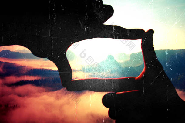 胶片颗粒。做框架的手势手的特写。蓝色迷雾笼罩的山谷贝娄岩石峰值。阳光明媚的春天黎明在洛矶山脉.