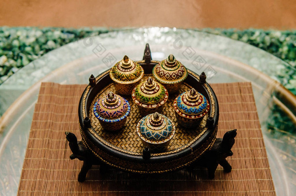传统的泰国著名瓷 benjarong 陶瓷装饰与大象站在藤表与玻璃表面与抽象的背景墙上下降水碗柳条板上。仪式.