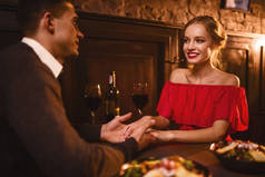 年轻的情侣在餐厅, 浪漫的约会。典雅的妇女在红色礼服和英俊的人用餐 