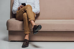 低段的年轻男子使用智能手机, 而坐在沙发上的灰色隔离