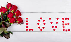 红玫瑰的花束和签名的爱由纸心在白色的背景, 复制空间。情人节、妇女节、母亲节的贺卡。爱, 婚礼概念, 平躺, 顶视图 