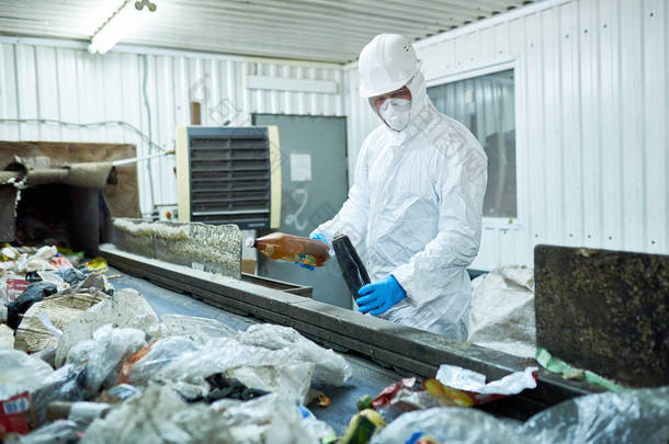 工人穿着生物危害服和安全帽工作在<strong>废物</strong>处理厂的肖像输送带可回收材料的分类