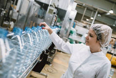 女工检查机器人生产线瓶装和包装纯净的饮用水瓶和罐