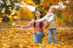 欢快的女孩玩黄叶。快乐的母亲和小孩子在秋天的时间有乐趣