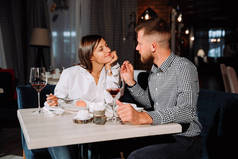 一对年轻夫妇在约会。一个男人给他的女人喂食美味的甜点。夫妇在餐馆笑