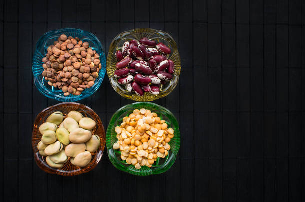 不同种类的豆类和扁豆在彩色的玻璃盘子上黑色的木材背景。饮食、体重控制和糖尿病的好处。豆类的健康益处.