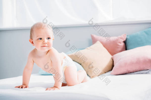 快乐的小宝宝爬在床上, 许多枕头和看着远离