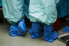 后台外科医生在手术室做手术。穿着防护鞋和长袍的外科医生