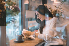 微笑的妇女读书在桌与咖啡杯子在咖啡馆