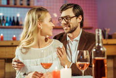 微笑的人在眼镜和夹克拥抱女朋友在桌子上的蜡烛在餐厅 