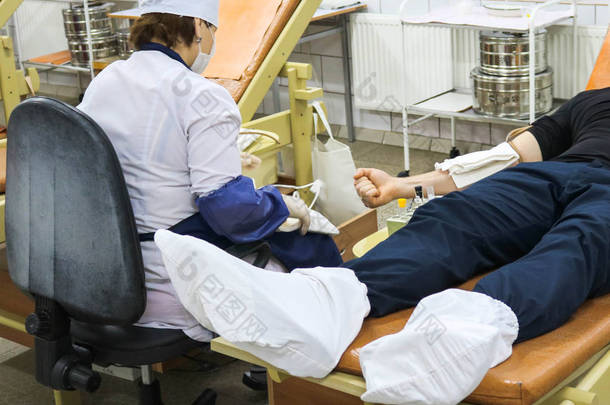 一位身穿白色外套的女医生从躺在医疗设施沙发上的捐献者身上取血