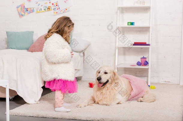 孩子在裙子看金毛猎犬躺在地毯上粉红色的裙子在儿童房