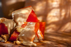 土耳其传统南瓜甜甜品塔特利西的碎片或立方体与核桃和芝麻酱塔欣在橄榄色的切割板上, 以傻瓜南瓜为背景..