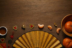 木桌上新鲜成熟的橘子、一杯茶、带象形文字和金币的扇子的顶视图 