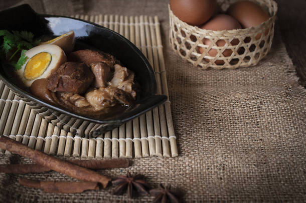煮鸡蛋和猪肉在黑色碗和香料地方在前面和篮子的蛋地方背面在木头筛子和 sack 和木头背景