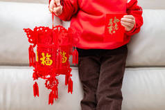 孩子拿着一个灯笼和一个红色的口袋过年, 文字翻译成灯笼上的英语财富, 一切都像红色口袋上的愿望一样