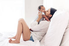 在家里的床上和婴儿一起玩耍的快乐微笑的母亲的肖像。对家庭概念的爱