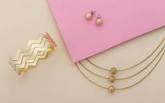 金色珠宝设置手镯和项链粉红色和米色背景